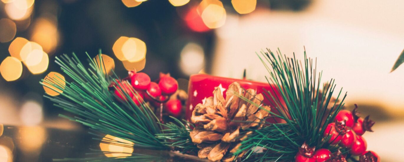 A vibrant Christmas scene with a red candle, pine cone, and berries, surrounded by holiday bokeh lights.