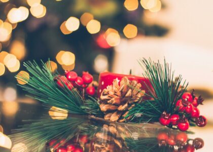 A vibrant Christmas scene with a red candle, pine cone, and berries, surrounded by holiday bokeh lights.