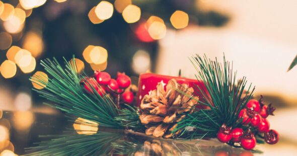 A vibrant Christmas scene with a red candle, pine cone, and berries, surrounded by holiday bokeh lights.